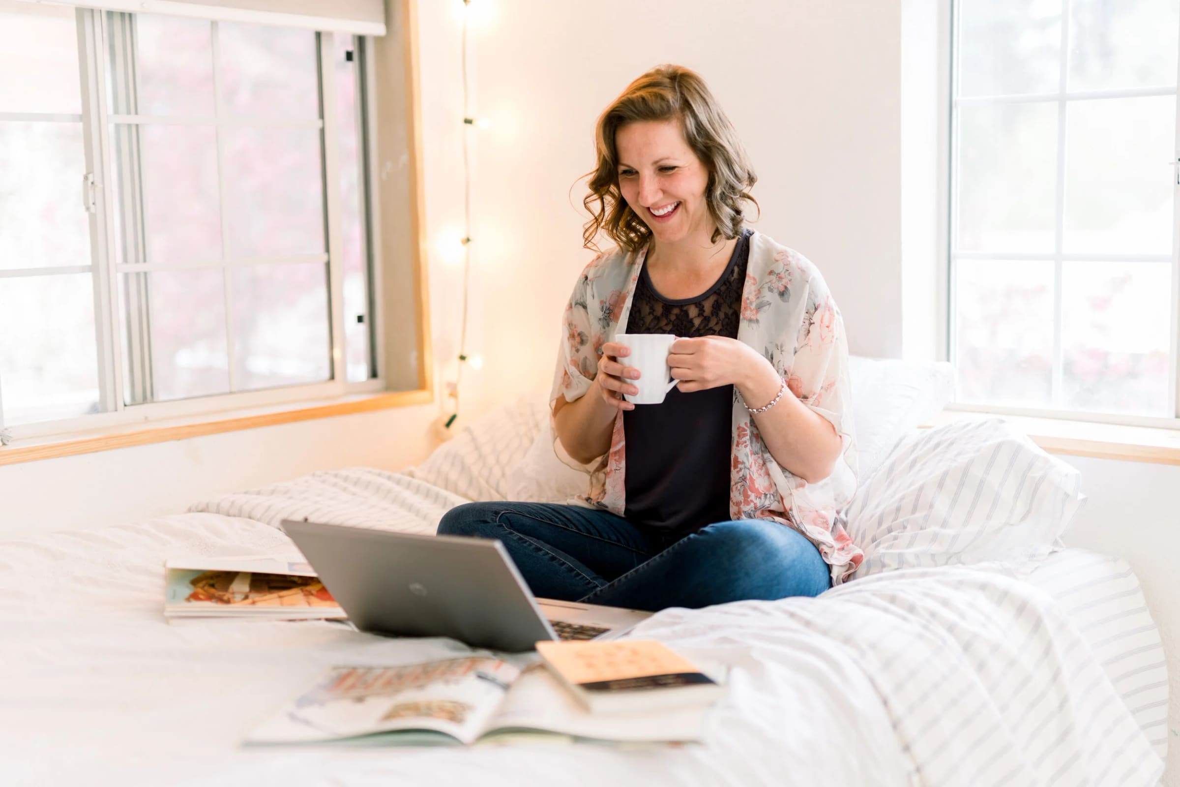 A business owner working from her bed with a laptop and open sketchbooks.