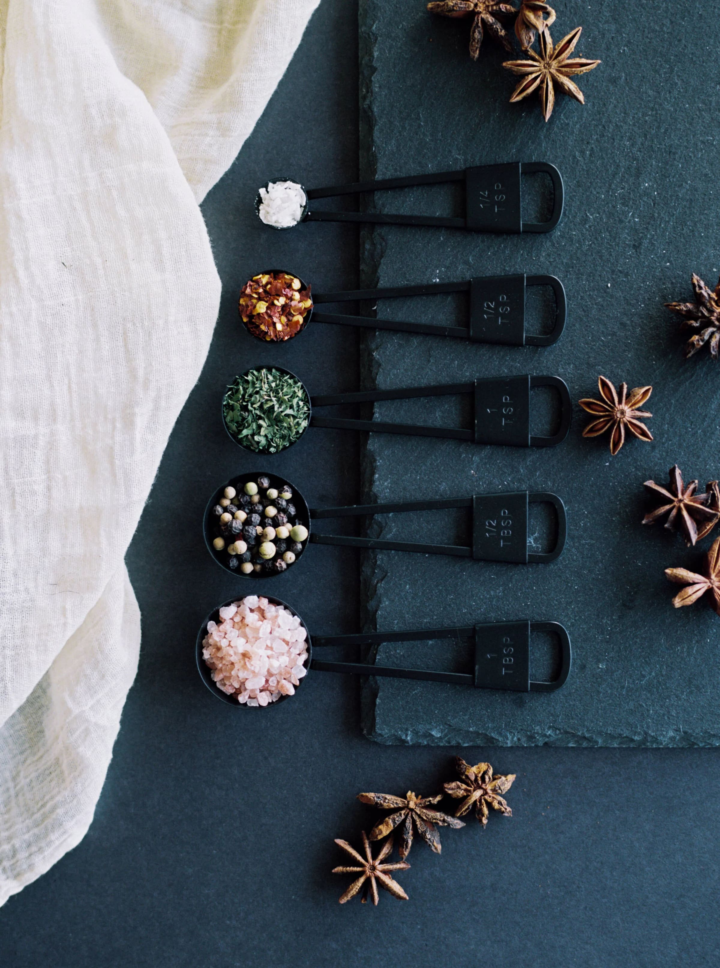 Overhead still life of measuring spoons filled with spices on slate.