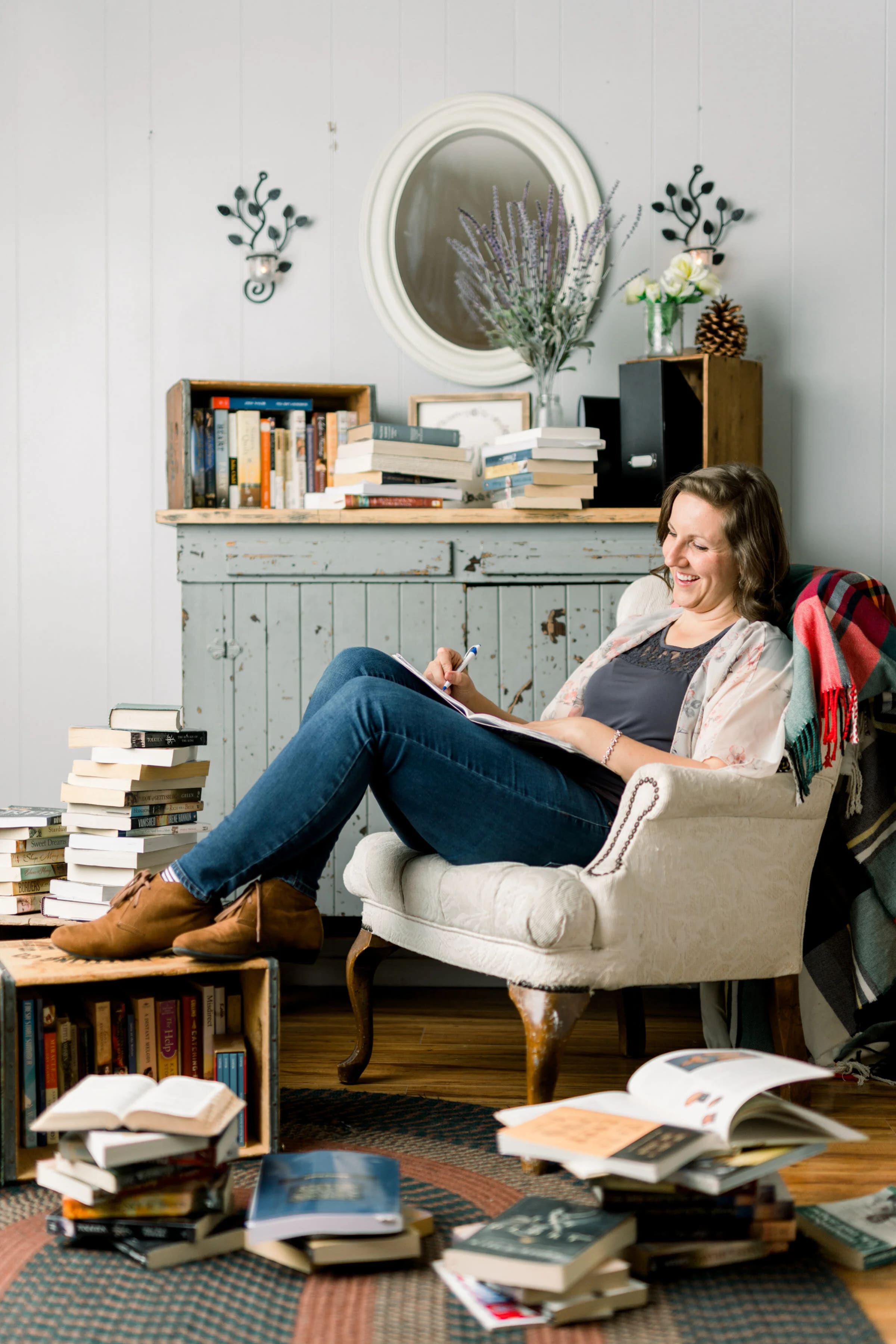 An author photographed at work in her studio, surrounded by stacks of books.